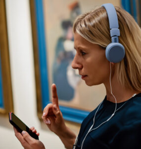 Museumsbesucherin mit Smartphone und Kopfhörer